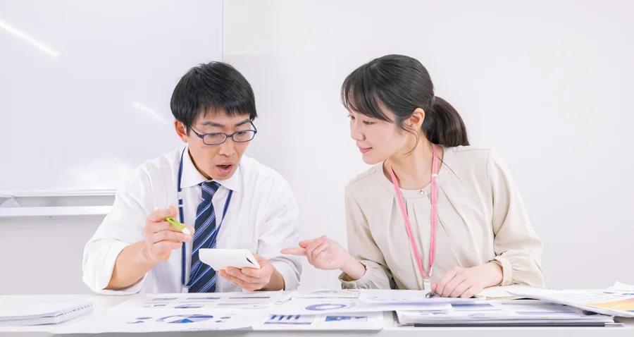 日本の明るい会議室で資料を説明し合う二人の業務イメージ